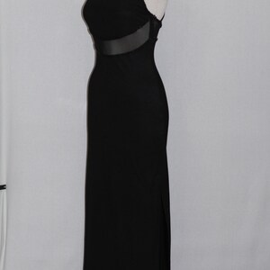 Pode incluir: Um vestido maxi preto com um painel de malha transparente na cintura. O vestido &eacute; sem mangas e tem uma fenda lateral.