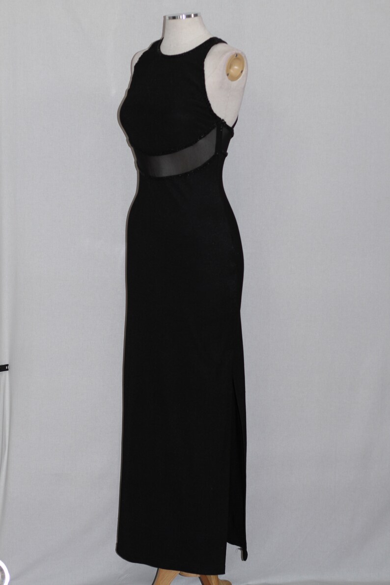 Pode incluir: Um vestido maxi preto com um painel de malha transparente na cintura. O vestido &eacute; sem mangas e tem uma fenda lateral.