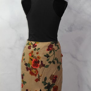 May include: A brown floral skirt with a slit in the back. The skirt has a floral pattern with red, orange, green, and brown flowers. The skirt is on a white mannequin.