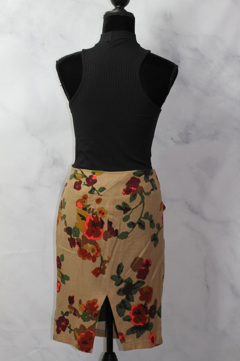 May include: A brown floral skirt with a slit in the back. The skirt has a floral pattern with red, orange, green, and brown flowers. The skirt is on a white mannequin.
