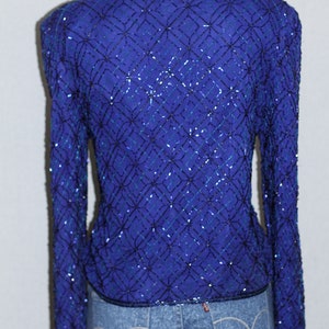 May include: A long-sleeved, sequined top in a deep blue color with a geometric pattern. The sequins are black and teal blue.