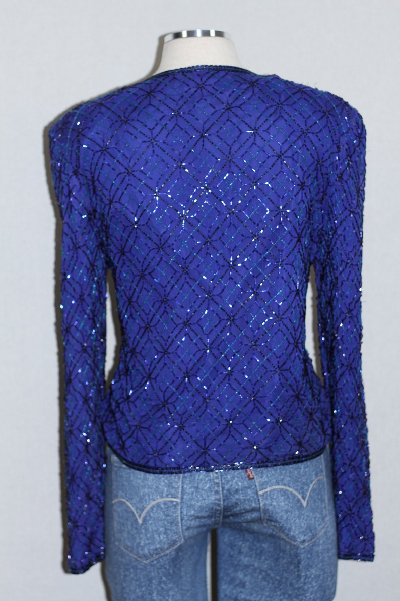 May include: A long-sleeved, sequined top in a deep blue color with a geometric pattern. The sequins are black and teal blue.