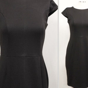 K&ouml;nnte beinhalten: Ein schwarzes Kleid mit kurzen &Auml;rmeln und einer figurbetonten Silhouette. Das Kleid hat einen runden Ausschnitt und ein schlichtes Design.