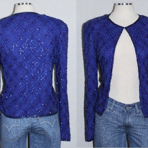 May include: A royal blue sequined jacket with long sleeves and an open front. The jacket is made of a soft, silky fabric and has a delicate, feminine look.