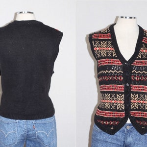 May include: Black sleeveless sweater vest with a red, beige, and black geometric pattern. The vest has a V-neck and a button closure.