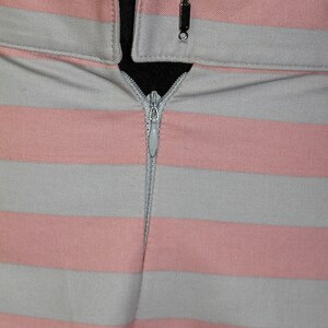 Puede incluir: Primer plano de una falda de rayas rosa y gris con cierre de cremallera. La cremallera est&aacute; cerrada y la falda est&aacute; hecha de una tela suave y tejida.