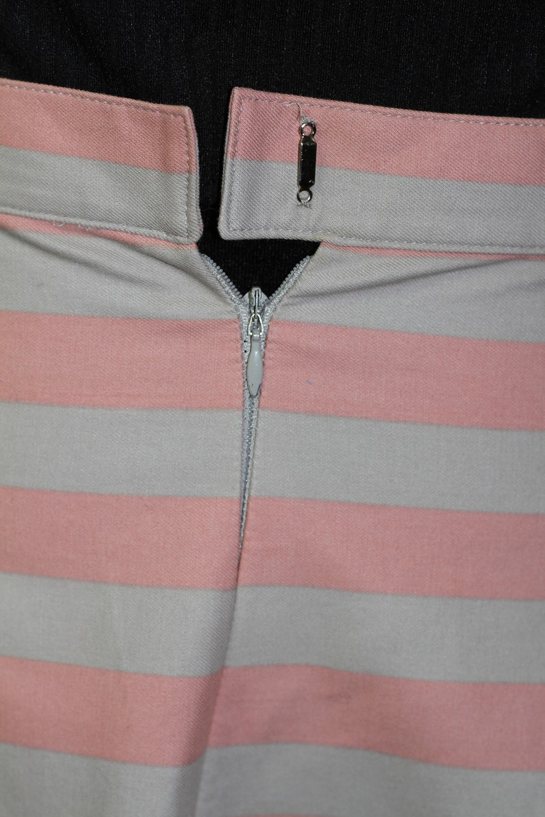 Puede incluir: Primer plano de una falda de rayas rosa y gris con cierre de cremallera. La cremallera est&aacute; cerrada y la falda est&aacute; hecha de una tela suave y tejida.