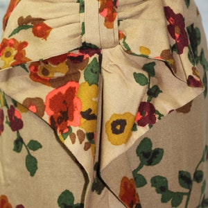 May include: A beige skirt with a floral print featuring red, orange, yellow, and green flowers. The skirt has a large bow at the waist.
