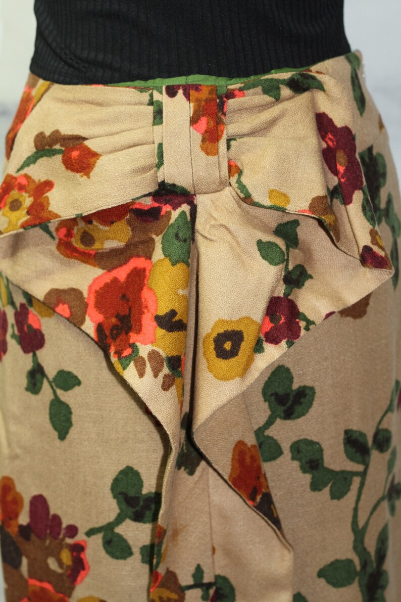 May include: A beige skirt with a floral print featuring red, orange, yellow, and green flowers. The skirt has a large bow at the waist.