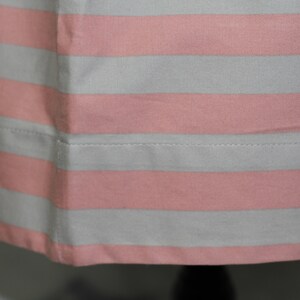 Puede incluir: Primer plano de una tela de rayas rosa y blancas con un dobladillo cosido. La tela es suave y tiene un brillo sutil.
