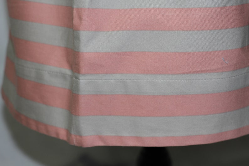 Puede incluir: Primer plano de una tela de rayas rosa y blancas con un dobladillo cosido. La tela es suave y tiene un brillo sutil.