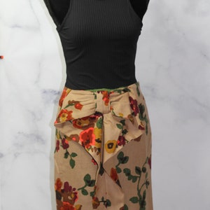 May include: A brown skirt with a floral print and a large bow at the waist. The skirt is on a mannequin wearing a black tank top.