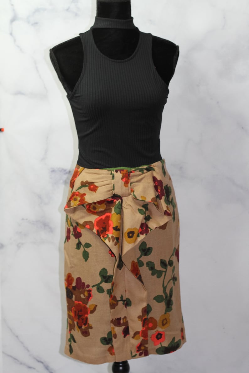 May include: A brown skirt with a floral print and a large bow at the waist. The skirt is on a mannequin wearing a black tank top.