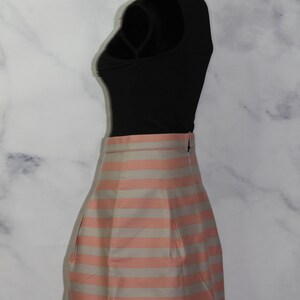 Puede incluir: Una falda de rayas rosa y blancas con un dise&ntilde;o plisado. La falda est&aacute; en un maniqu&iacute; y es de longitud midi.