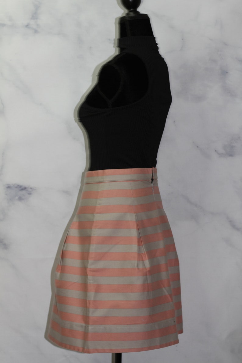 Puede incluir: Una falda de rayas rosa y blancas con un dise&ntilde;o plisado. La falda est&aacute; en un maniqu&iacute; y es de longitud midi.