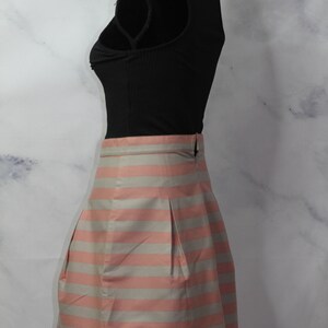 Puede incluir: Una falda de rayas rosa y grises con un dise&ntilde;o plisado. La falda es de largo hasta la rodilla y tiene una cintura ajustada.