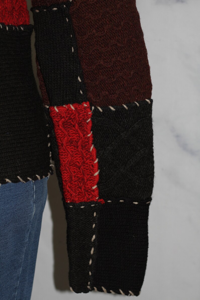 K&ouml;nnte beinhalten: Nahaufnahme eines rot, schwarz und braunen Strickpullovers mit Patchwork-Muster. Der Pullover hat ein Zopfmuster und ist mit wei&szlig;em Garn zusammengen&auml;ht.