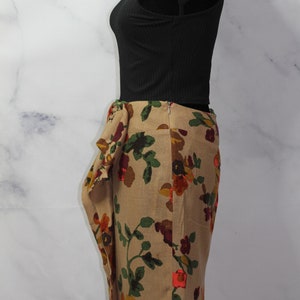 May include: A beige skirt with a floral print featuring red, orange, and green flowers. The skirt has a gathered detail at the waist and a fitted silhouette.