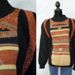 Op de afbeelding: Een zwarte trui met een kleurrijk geometrisch patroon in tinten bruin, oranje en beige. De trui heeft een mock neck en lange mouwen.