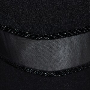 Pode incluir: Tecido preto com um painel transparente e uma guarni&ccedil;&atilde;o de contas. A guarni&ccedil;&atilde;o &eacute; feita de pequenas contas pretas.