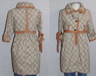 Könnte beinhalten: Ein beiger Trenchcoat mit einem braunen Ledergürtel und einem Seilmuster. Der Mantel hat einen Kragen und lange Ärmel.