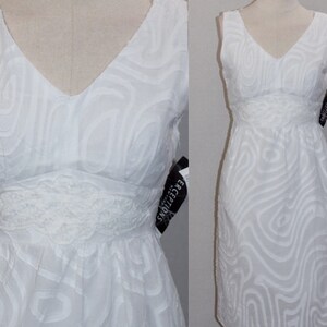May include: White sleeveless dress with a V-neckline and a lace trim at the waist. The dress has a swirling pattern and is made of a lightweight fabric.