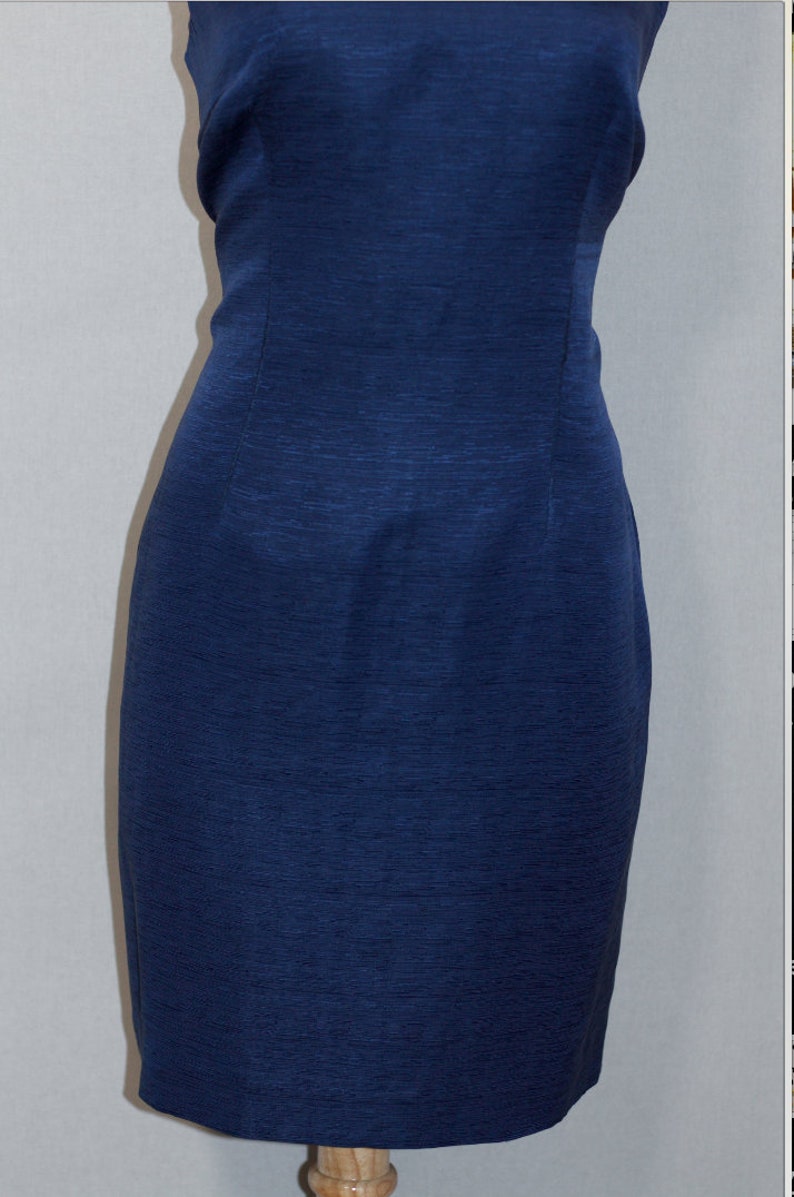 May include: A sleeveless, navy blue dress with a fitted silhouette. The dress is made of a textured fabric and has a simple, elegant design.