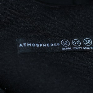K&ouml;nnte beinhalten: Ein schwarzes Kleidungsetikett mit wei&szlig;em Text, der "ATMOSPHERE&reg; 12 40 38 UK/IRL ES/PT D/NL/B/A" lautet.