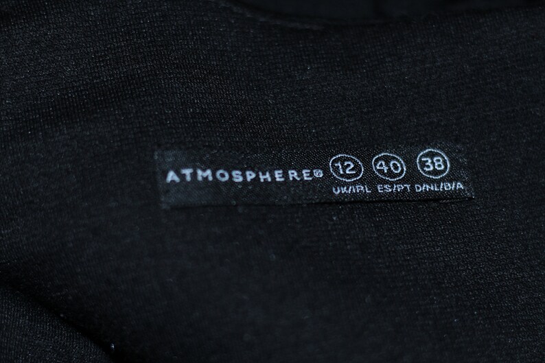 K&ouml;nnte beinhalten: Ein schwarzes Kleidungsetikett mit wei&szlig;em Text, der "ATMOSPHERE&reg; 12 40 38 UK/IRL ES/PT D/NL/B/A" lautet.