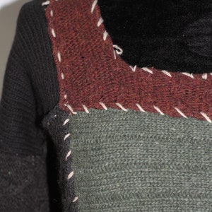 K&ouml;nnte beinhalten: Nahaufnahme eines Pullovers mit Patchwork-Design. Der Pullover besteht aus verschiedenenfarbigen Garnen, darunter Schwarz, Braun und Gr&uuml;n. Die N&auml;hte sind sichtbar und mit wei&szlig;em Garn gen&auml;ht.