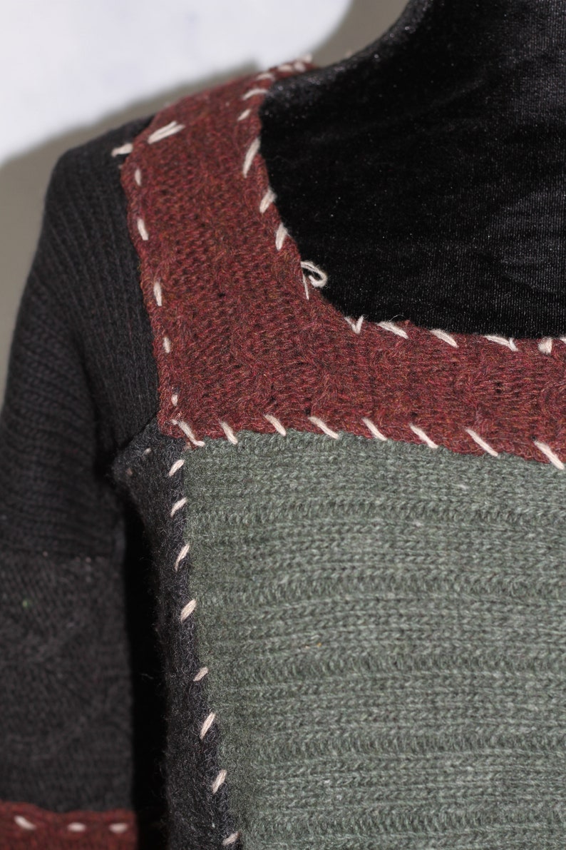 K&ouml;nnte beinhalten: Nahaufnahme eines Pullovers mit Patchwork-Design. Der Pullover besteht aus verschiedenenfarbigen Garnen, darunter Schwarz, Braun und Gr&uuml;n. Die N&auml;hte sind sichtbar und mit wei&szlig;em Garn gen&auml;ht.