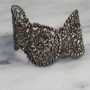 May include: A silver metal bracelet with a floral design. The bracelet is made of small beads and has a delicate, intricate pattern.