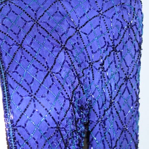 May include: A close-up of a blue beaded fabric with a geometric pattern. The beads are arranged in a grid pattern, creating a diamond shape. The fabric is soft and luxurious, and the beads are iridescent, catching the light.
