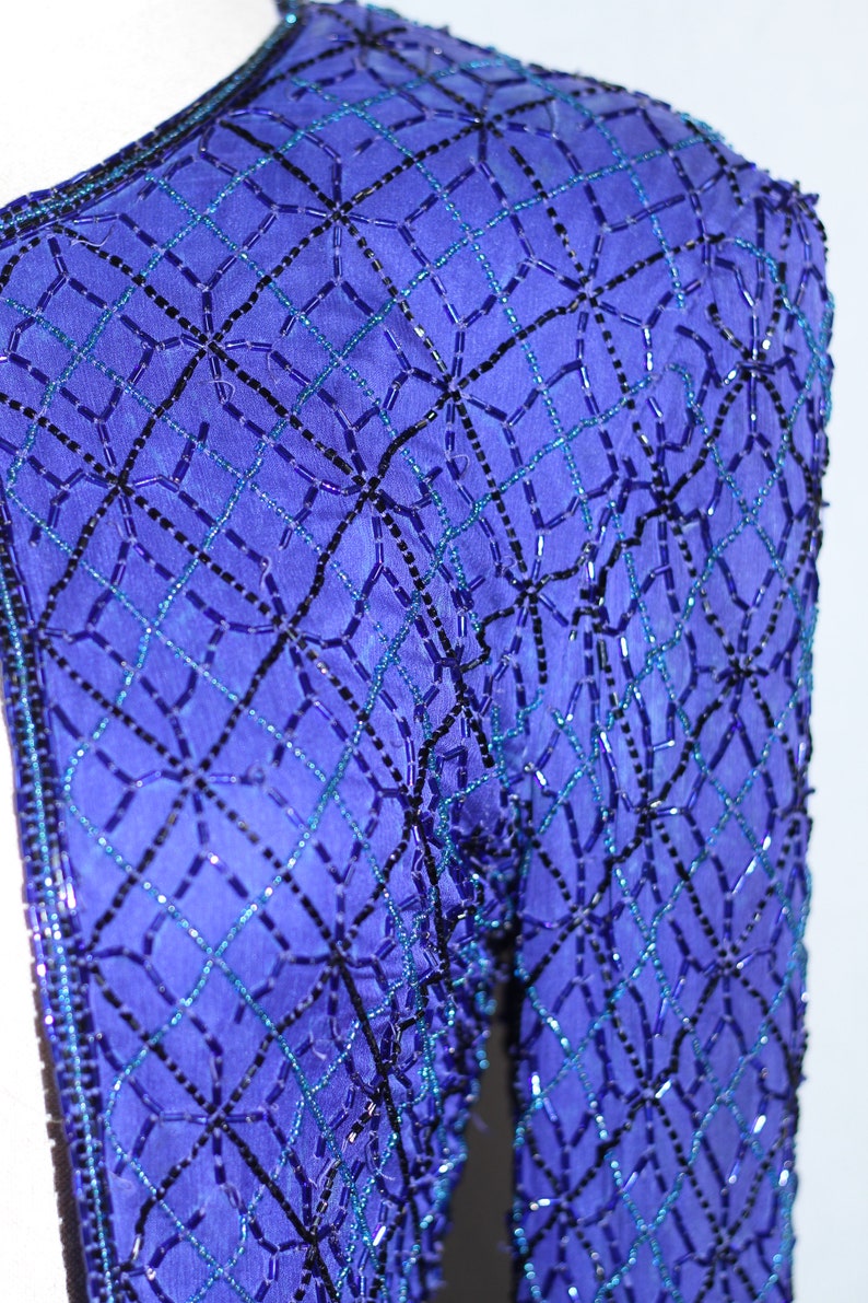 May include: A close-up of a blue beaded fabric with a geometric pattern. The beads are arranged in a grid pattern, creating a diamond shape. The fabric is soft and luxurious, and the beads are iridescent, catching the light.