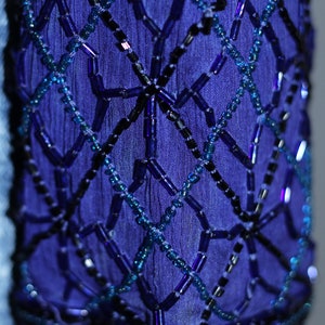 May include: Close-up of a blue fabric with a geometric pattern of black and blue beads.