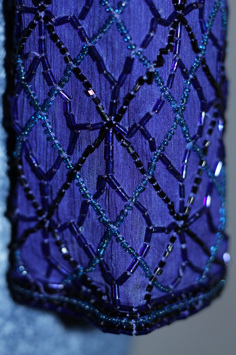 May include: Close-up of a blue fabric with a geometric pattern of black and blue beads.