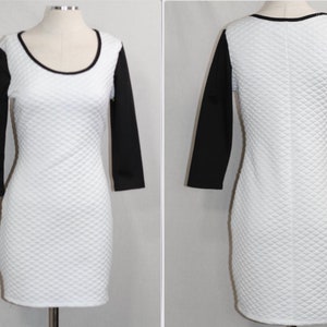 May include: A white, quilted-patterned dress with black, three-quarter sleeves. The dress has a scoop neckline and a black trim. The dress is displayed on a mannequin. The dress is a bodycon style.