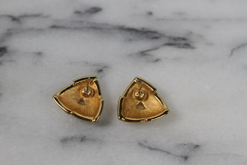 May include: A pair of gold-tone triangle shaped earrings with a textured surface.
