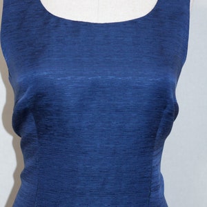 May include: A sleeveless, dark blue dress with a scoop neckline. The dress is made of a textured fabric.