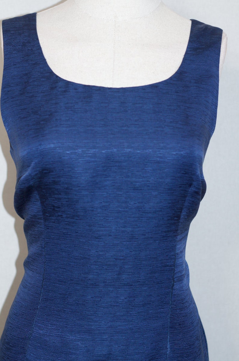 May include: A sleeveless, dark blue dress with a scoop neckline. The dress is made of a textured fabric.