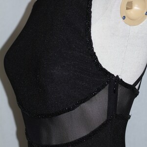 Pode incluir: Vestido preto sem mangas com um painel de malha e acabamento de contas. O vestido tem um decote redondo e uma silhueta ajustada.