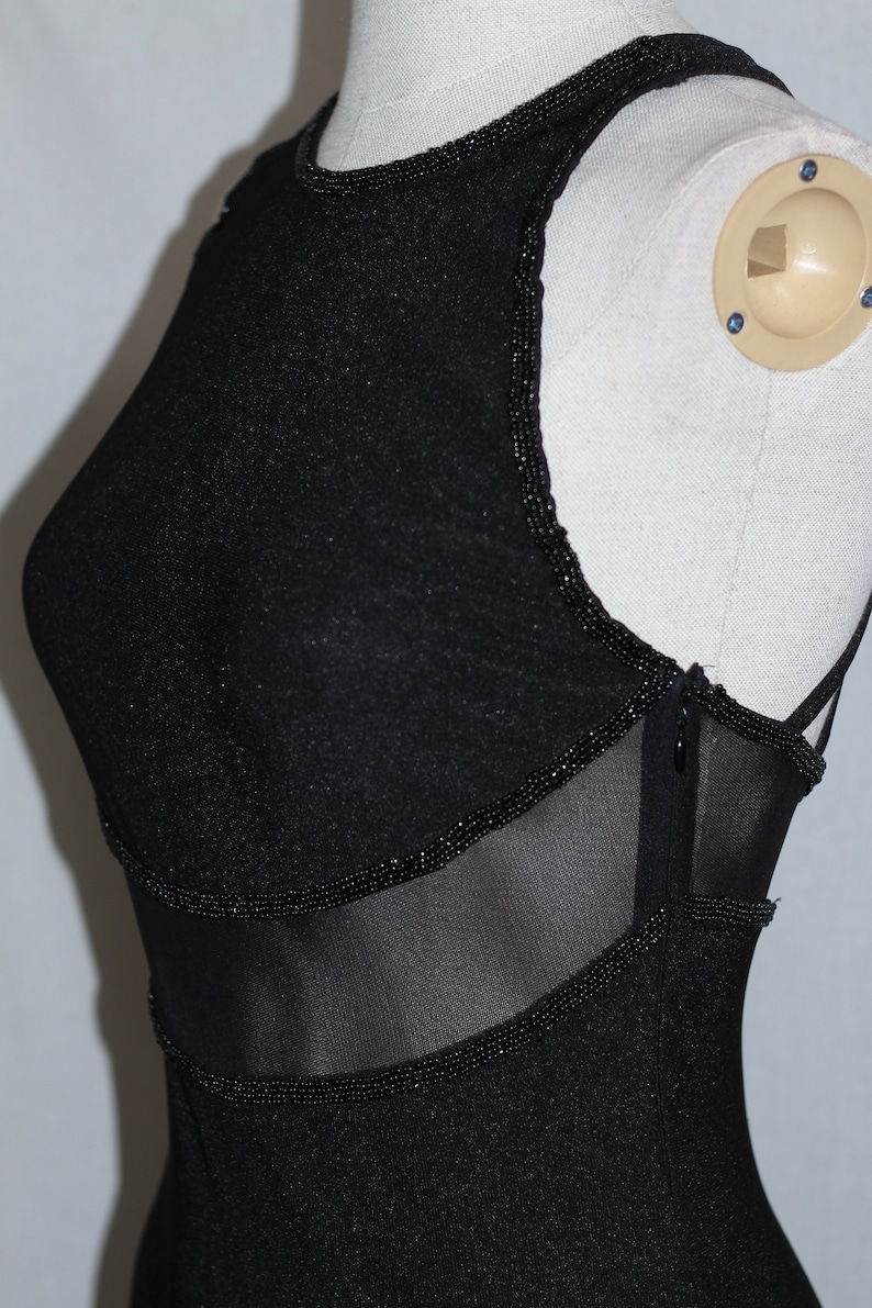 Pode incluir: Vestido preto sem mangas com um painel de malha e acabamento de contas. O vestido tem um decote redondo e uma silhueta ajustada.