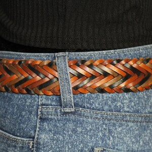 K&ouml;nnte beinhalten: Ein geflochtener Lederg&uuml;rtel mit braunen, schwarzen und braunen Lederstr&auml;ngen. Der G&uuml;rtel ist im Fischgr&auml;tenmuster gewebt.