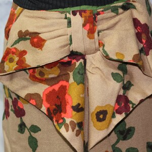 May include: A beige skirt with a large bow in the back. The skirt has a floral print with red, orange, yellow, and green flowers.