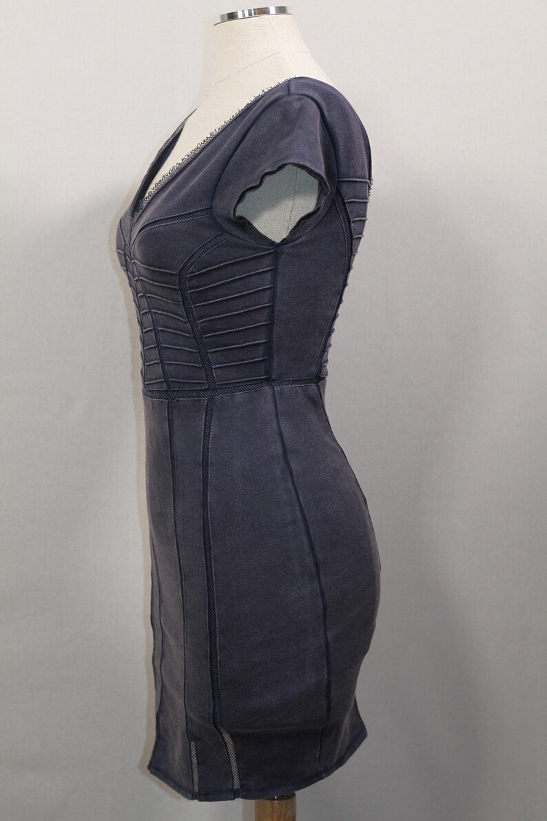 K&ouml;nnte beinhalten: Ein dunkelgraues, figurbetontes Kleid mit V-Ausschnitt und kurzen &Auml;rmeln. Das Kleid hat eine strukturierte, leicht abgenutzte Optik und ist mit dekorativen N&auml;hten versehen.