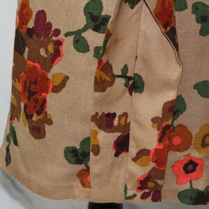 May include: A beige fabric with a floral print featuring orange, red, brown, and green flowers. The fabric has a seam down the center.
