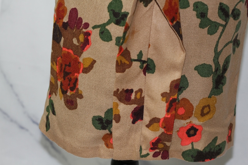 May include: A beige fabric with a floral print featuring orange, red, brown, and green flowers. The fabric has a seam down the center.