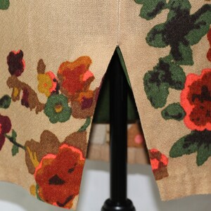 May include: A beige skirt with a floral print featuring red, orange, green, and brown flowers. The skirt has a slit up the back.