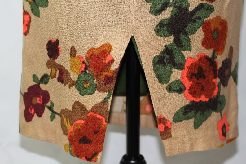 May include: A beige skirt with a floral print featuring red, orange, green, and brown flowers. The skirt has a slit up the back.