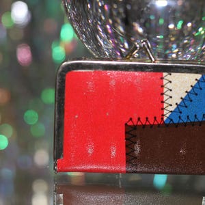 May include: A small, red, brown, white, and blue patchwork wallet with a silver metal frame.